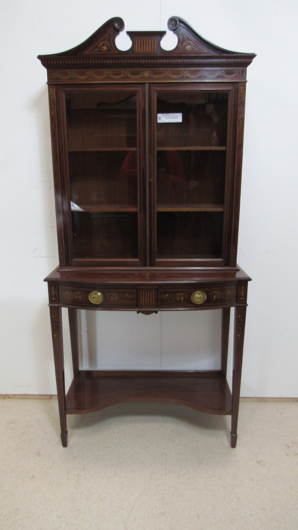 An Edwardian dark mahogany display cabinet featuring a swan-neck pediment, delicate satinwood floral marquetry, two glazed upper doors, drawers with brass handles, and tapered legs with an undertier shelf. View V