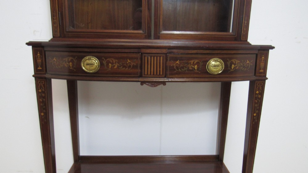 An Edwardian dark mahogany display cabinet featuring a swan-neck pediment, delicate satinwood floral marquetry, two glazed upper doors, drawers with brass handles, and tapered legs with an undertier shelf. View VII