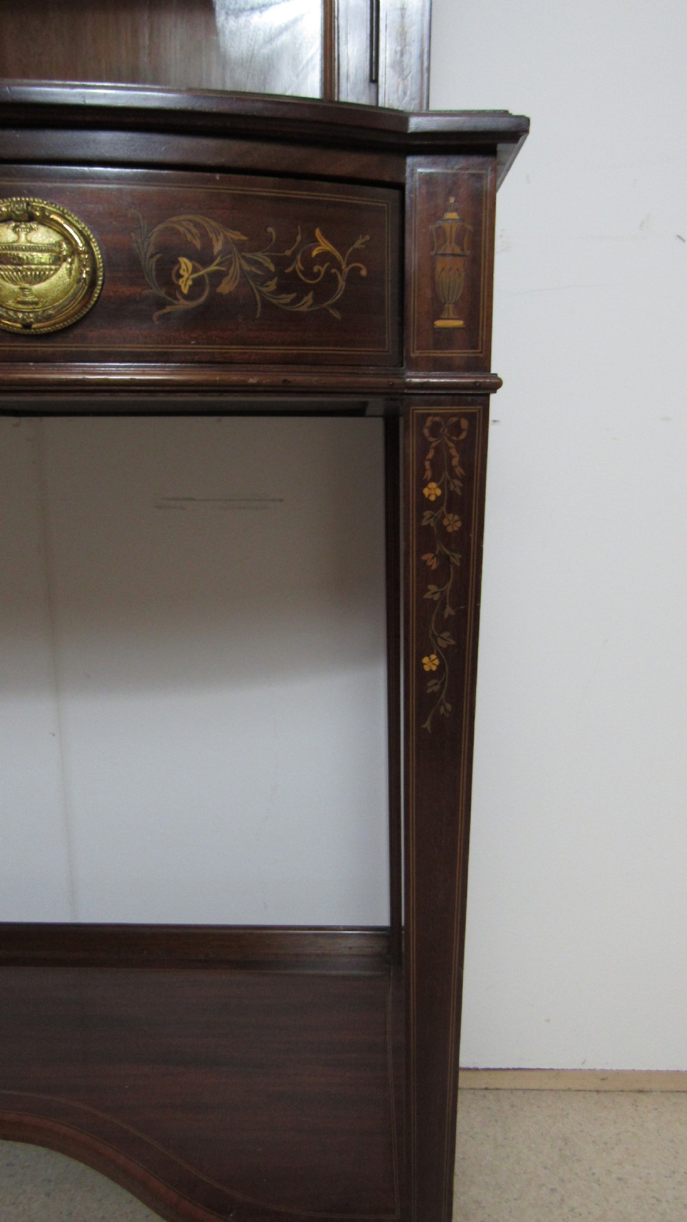 An Edwardian dark mahogany display cabinet featuring a swan-neck pediment, delicate satinwood floral marquetry, two glazed upper doors, drawers with brass handles, and tapered legs with an undertier shelf. View VIII