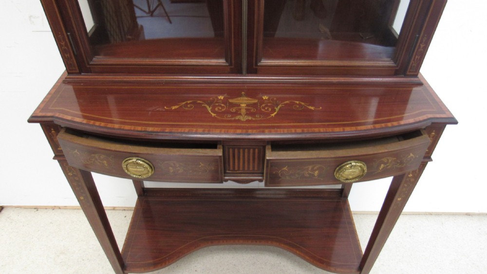 An Edwardian dark mahogany display cabinet featuring a swan-neck pediment, delicate satinwood floral marquetry, two glazed upper doors, drawers with brass handles, and tapered legs with an undertier shelf. View XI