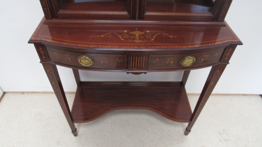 An Edwardian dark mahogany display cabinet featuring a swan-neck pediment, delicate satinwood floral marquetry, two glazed upper doors, drawers with brass handles, and tapered legs with an undertier shelf. View XII