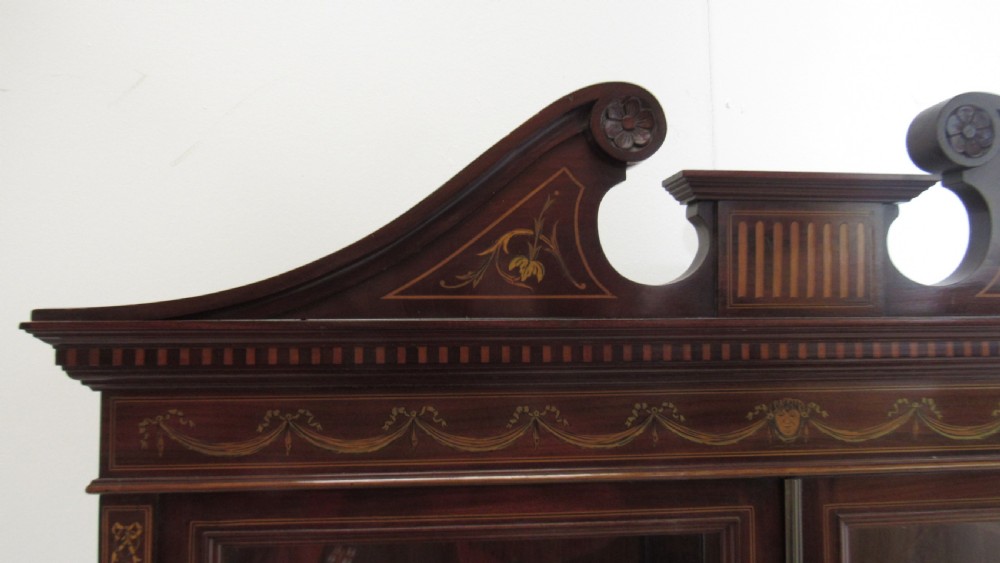 An Edwardian dark mahogany display cabinet featuring a swan-neck pediment, delicate satinwood floral marquetry, two glazed upper doors, drawers with brass handles, and tapered legs with an undertier shelf. View XIV