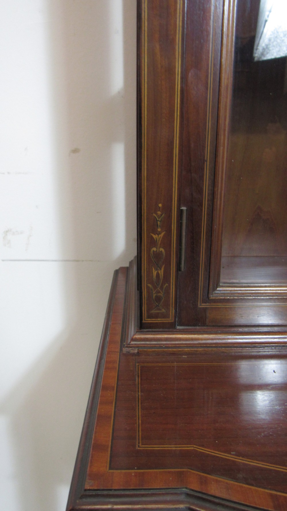 An Edwardian dark mahogany display cabinet featuring a swan-neck pediment, delicate satinwood floral marquetry, two glazed upper doors, drawers with brass handles, and tapered legs with an undertier shelf. View XVII