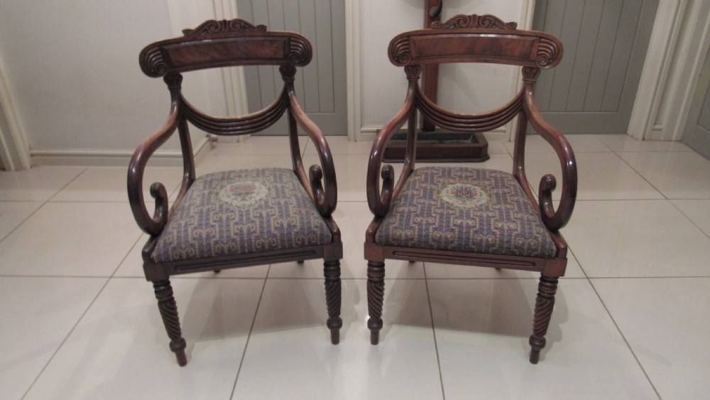 Pair of Regency mahogany carver chairs featuring curved scroll arms, reeded front legs, and patterned fabric seat upholstery.