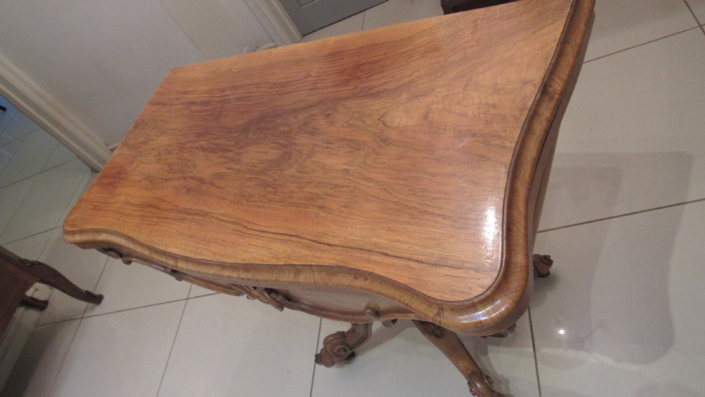 An antique Victorian walnut card table featuring a serpentine fold-over top resting on a carved central pedestal and scroll feet. View II