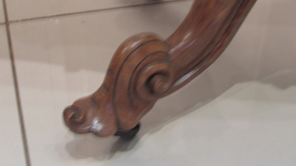 An antique Victorian walnut card table featuring a serpentine fold-over top resting on a carved central pedestal and scroll feet. View VI