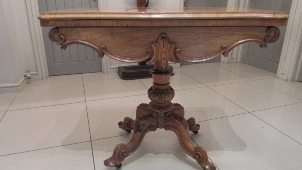 An antique Victorian walnut card table featuring a serpentine fold-over top resting on a carved central pedestal and scroll feet. View IX