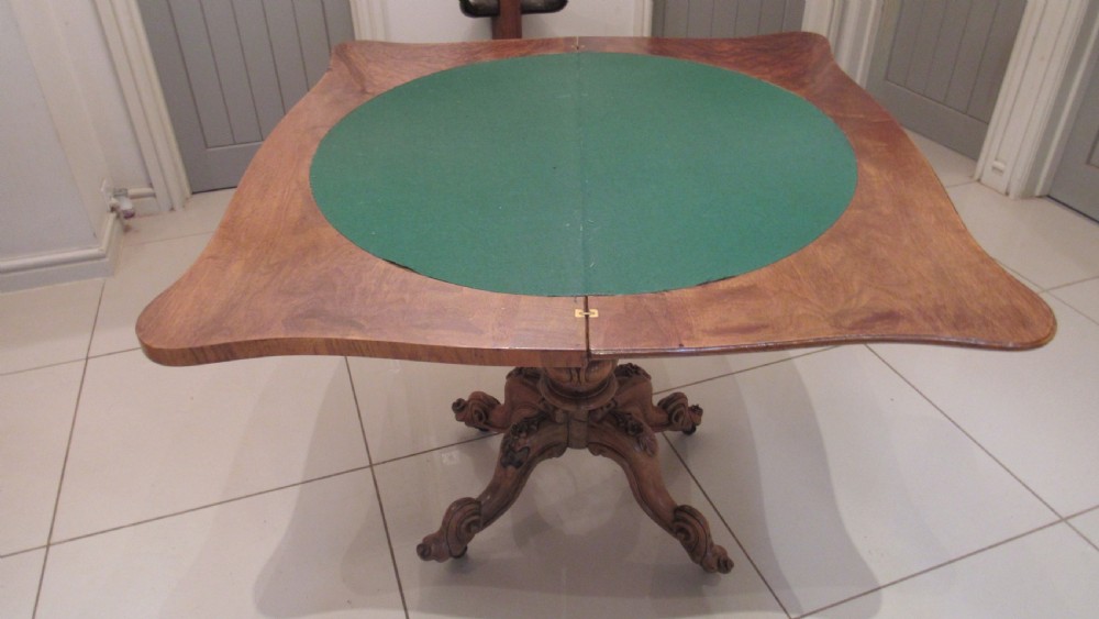 An antique Victorian walnut card table featuring a serpentine fold-over top resting on a carved central pedestal and scroll feet. View X