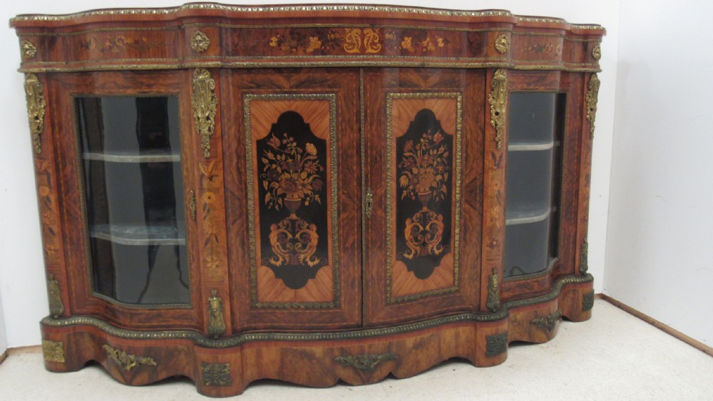 A Victorian serpentine-front credenza featuring central floral marquetry doors, glass display side cupboards, and ornate gilt-bronze mounts.