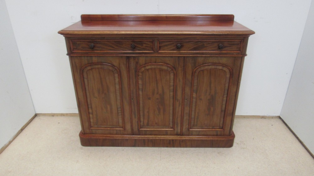 A Victorian mahogany side cabinet with a low rear gallery, two upper drawers, and three arched panel cupboard doors set on a plinth base.