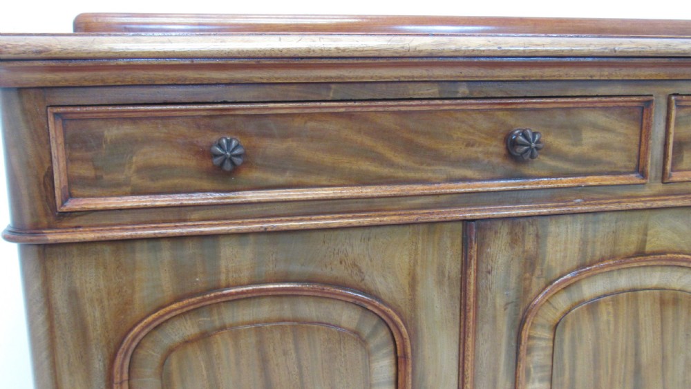 A Victorian mahogany side cabinet with a low rear gallery, two upper drawers, and three arched panel cupboard doors set on a plinth base. View V