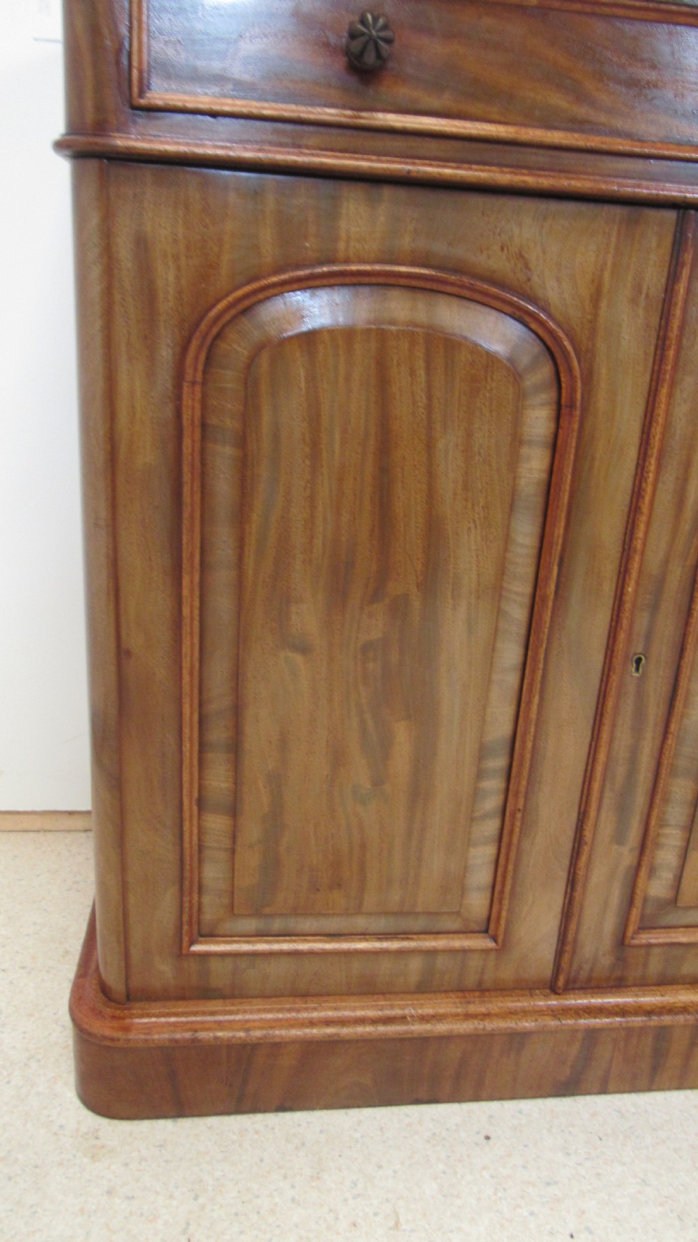 A Victorian mahogany side cabinet with a low rear gallery, two upper drawers, and three arched panel cupboard doors set on a plinth base. View VI