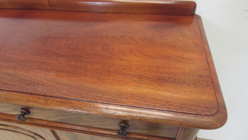 A Victorian mahogany side cabinet with a low rear gallery, two upper drawers, and three arched panel cupboard doors set on a plinth base. View VII