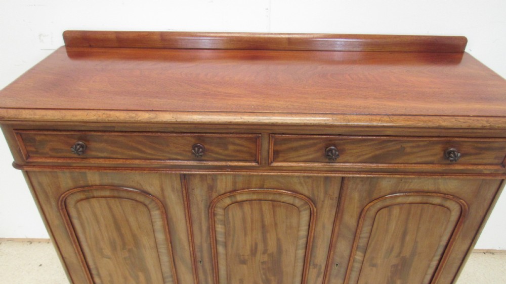 A Victorian mahogany side cabinet with a low rear gallery, two upper drawers, and three arched panel cupboard doors set on a plinth base. View VIII