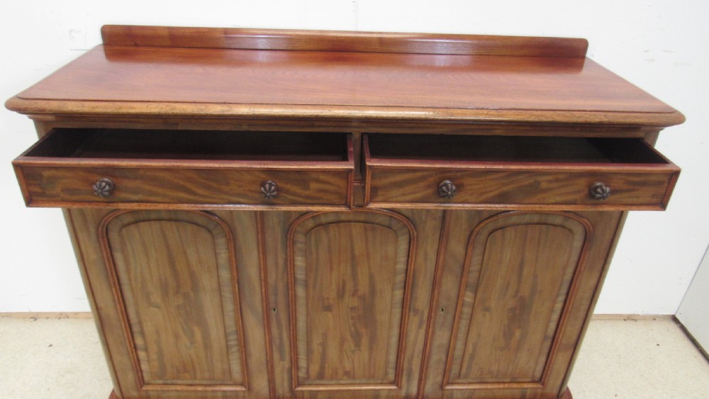 A Victorian mahogany side cabinet with a low rear gallery, two upper drawers, and three arched panel cupboard doors set on a plinth base. View IX
