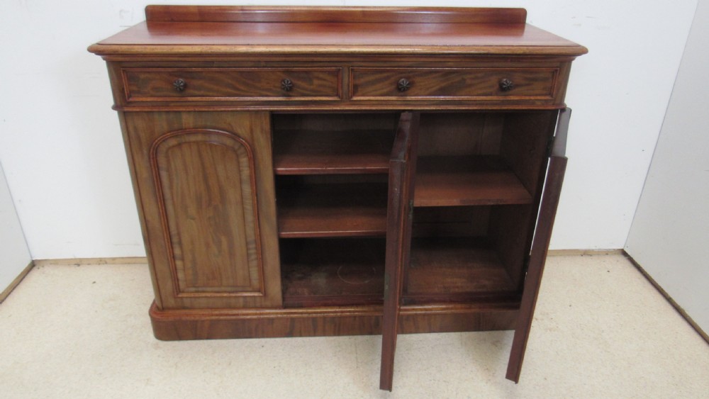 A Victorian mahogany side cabinet with a low rear gallery, two upper drawers, and three arched panel cupboard doors set on a plinth base. View X
