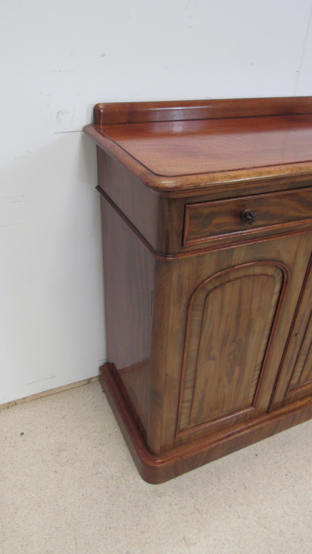 A Victorian mahogany side cabinet with a low rear gallery, two upper drawers, and three arched panel cupboard doors set on a plinth base. View XV