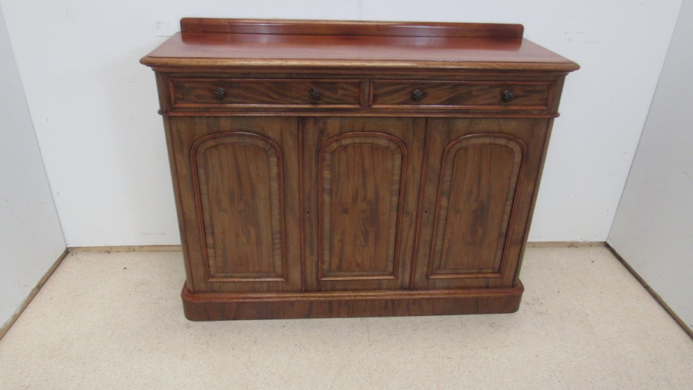 A Victorian mahogany side cabinet with a low rear gallery, two upper drawers, and three arched panel cupboard doors set on a plinth base. View XVI