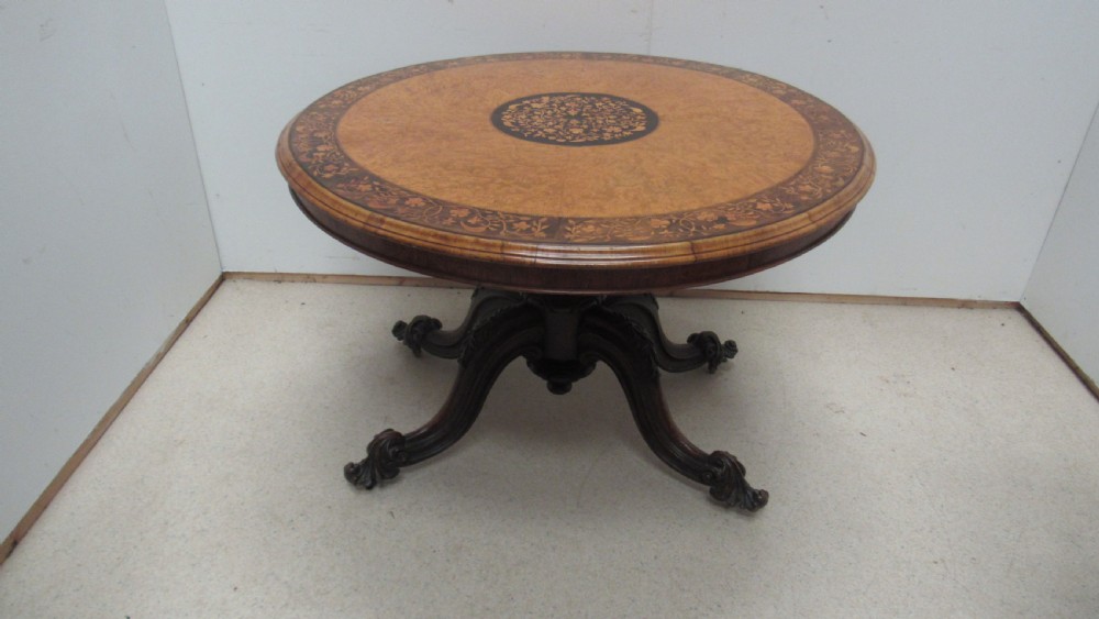 A circular Victorian walnut occasional table featuring intricate floral marquetry inlay along the border and central medallion, supported on a carved tripod pedestal base. View II