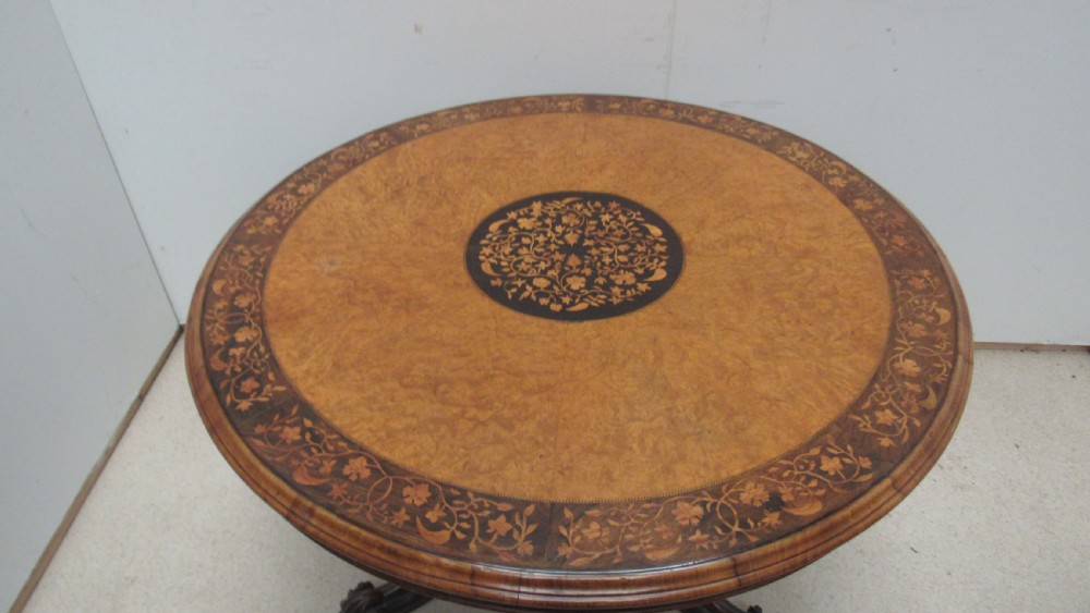 A circular Victorian walnut occasional table featuring intricate floral marquetry inlay along the border and central medallion, supported on a carved tripod pedestal base. View V