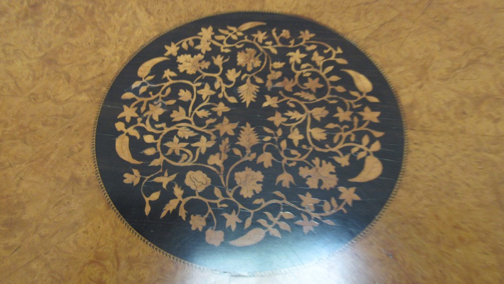 A circular Victorian walnut occasional table featuring intricate floral marquetry inlay along the border and central medallion, supported on a carved tripod pedestal base. View VI