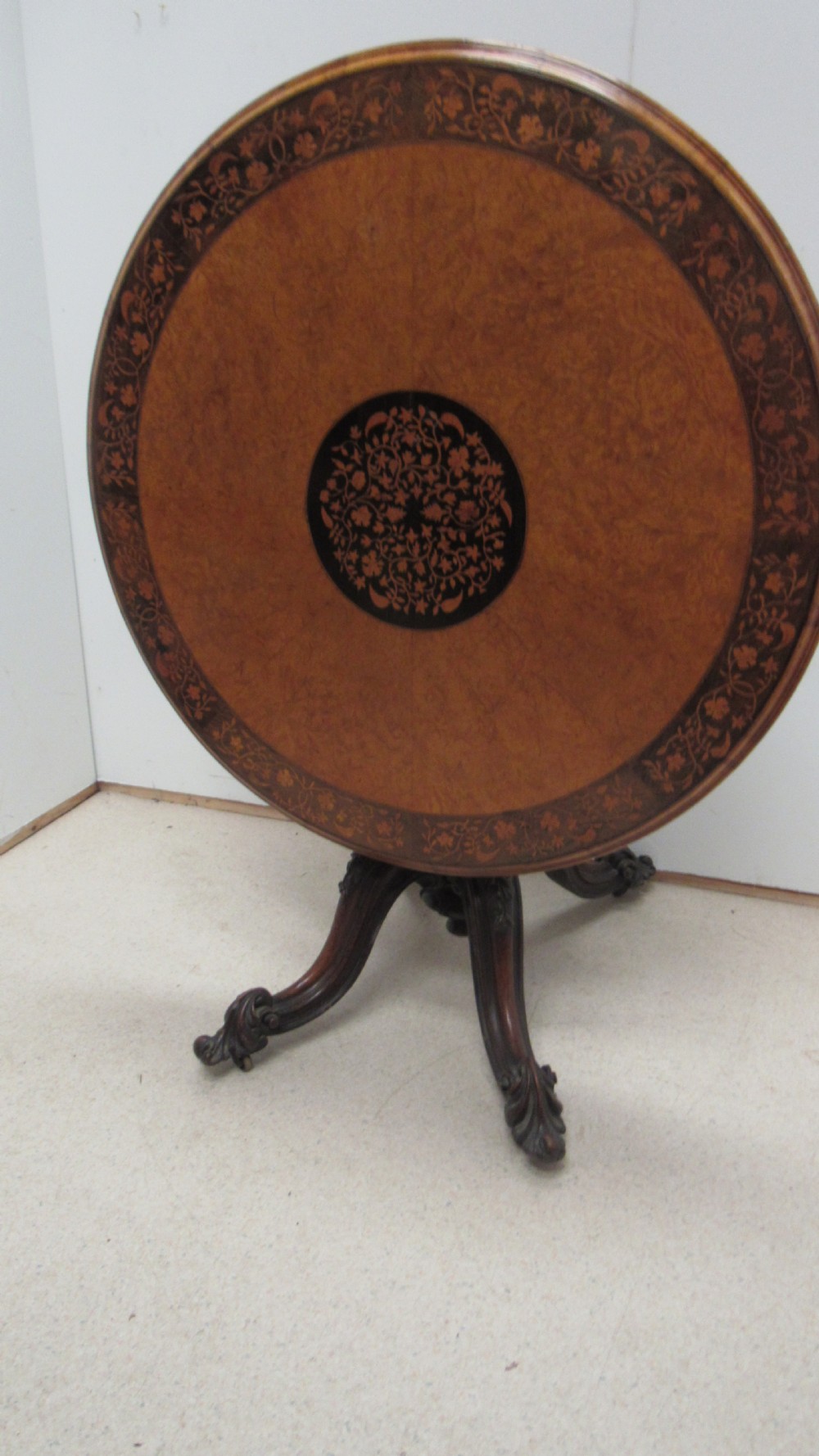 A circular Victorian walnut occasional table featuring intricate floral marquetry inlay along the border and central medallion, supported on a carved tripod pedestal base. View X