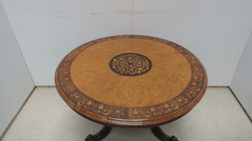 A circular Victorian walnut occasional table featuring intricate floral marquetry inlay along the border and central medallion, supported on a carved tripod pedestal base. View XVII