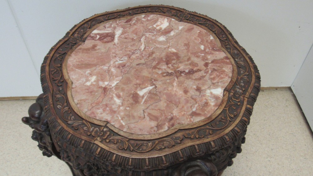 A circular dark wood urn stand featuring an inset pink marble top, detailed relief carving on the apron, curved cabriole legs, and a lower shelf. View II