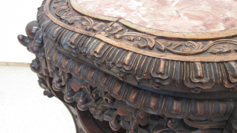 A circular dark wood urn stand featuring an inset pink marble top, detailed relief carving on the apron, curved cabriole legs, and a lower shelf. View VI