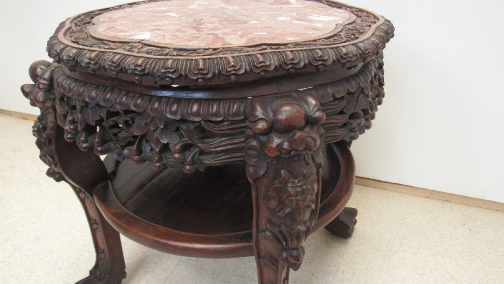 A circular dark wood urn stand featuring an inset pink marble top, detailed relief carving on the apron, curved cabriole legs, and a lower shelf. View VII