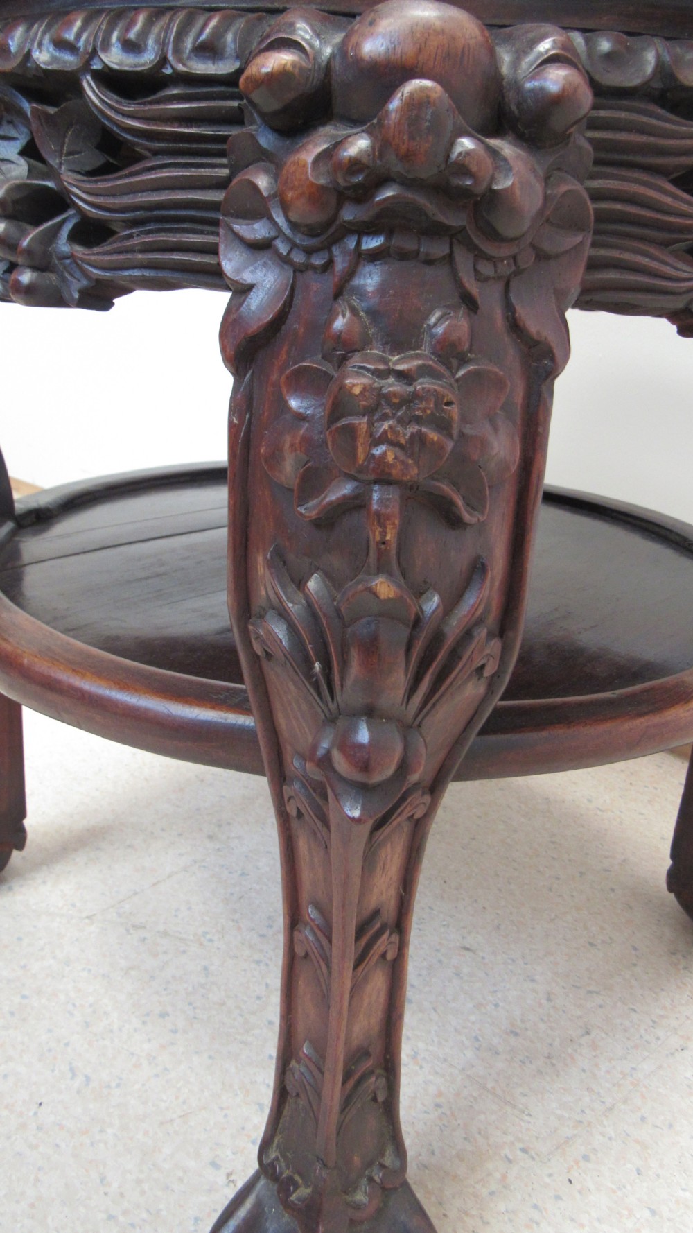 A circular dark wood urn stand featuring an inset pink marble top, detailed relief carving on the apron, curved cabriole legs, and a lower shelf. View X