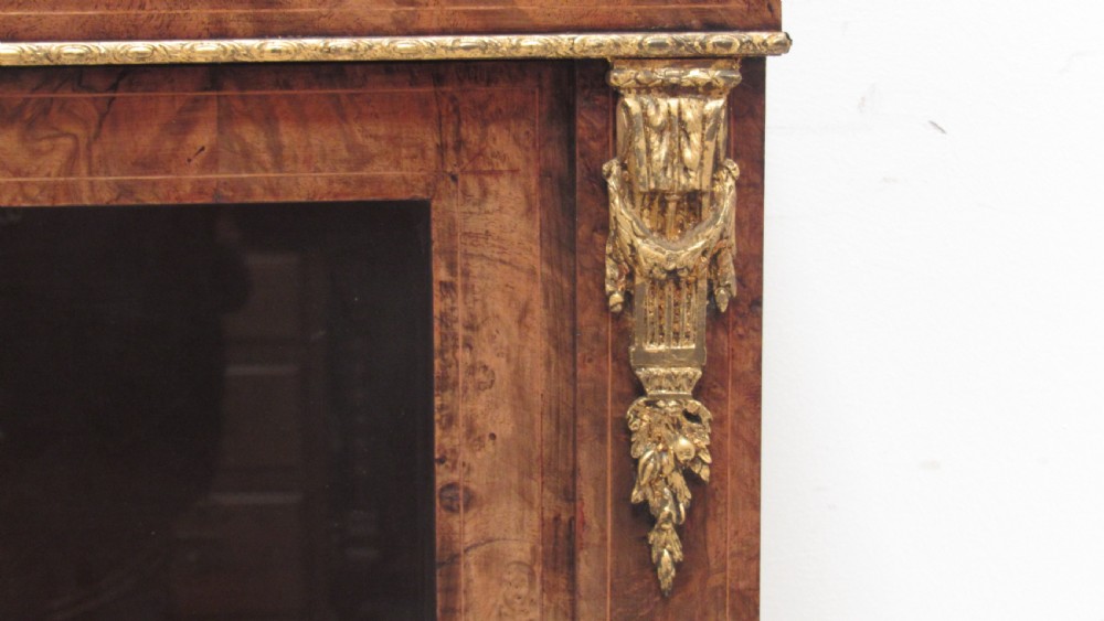 A 19th-century Victorian burr walnut pier cabinet featuring floral marquetry inlay, glazed double doors, glass shelves, and gilt brass corner mounts. View II