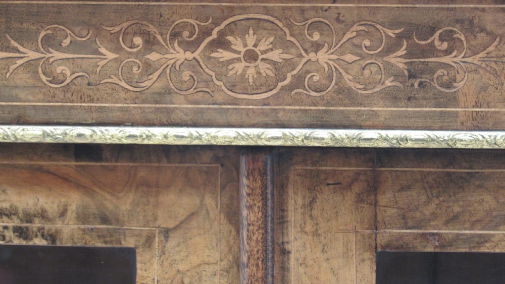 A 19th-century Victorian burr walnut pier cabinet featuring floral marquetry inlay, glazed double doors, glass shelves, and gilt brass corner mounts. View III