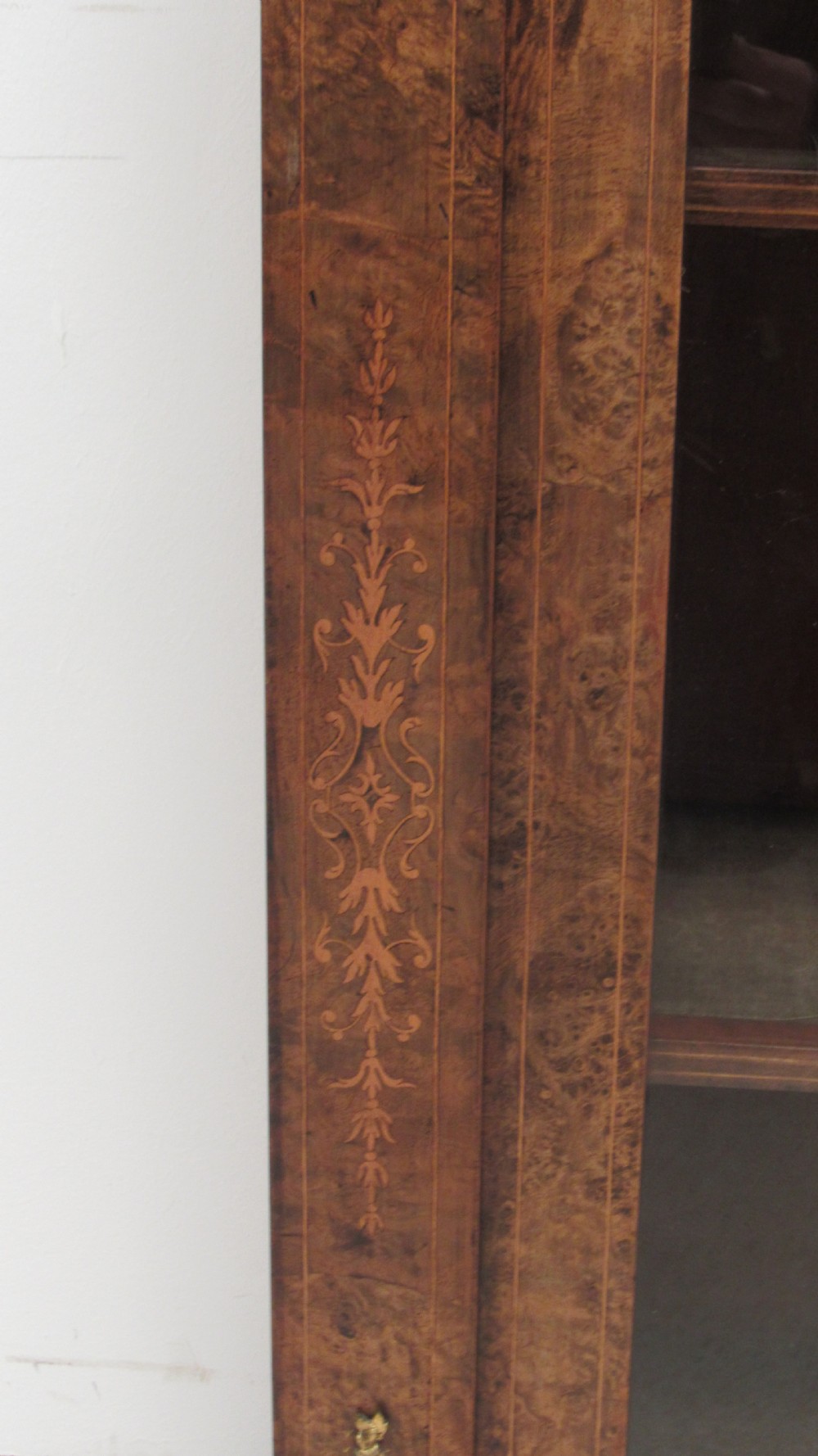 A 19th-century Victorian burr walnut pier cabinet featuring floral marquetry inlay, glazed double doors, glass shelves, and gilt brass corner mounts. View V
