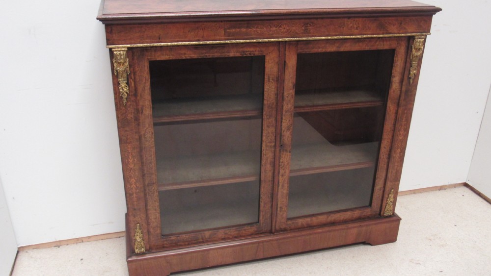 A 19th-century Victorian burr walnut pier cabinet featuring floral marquetry inlay, glazed double doors, glass shelves, and gilt brass corner mounts. View XIV