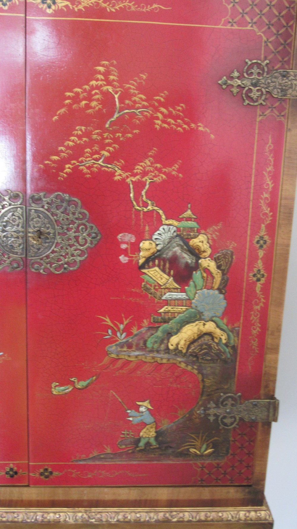 A red lacquered chinoiserie cocktail cabinet decorated with gilt landscapes and figures, featuring ornate brass hinges and set on a carved timber stand with cabriole legs. View IX