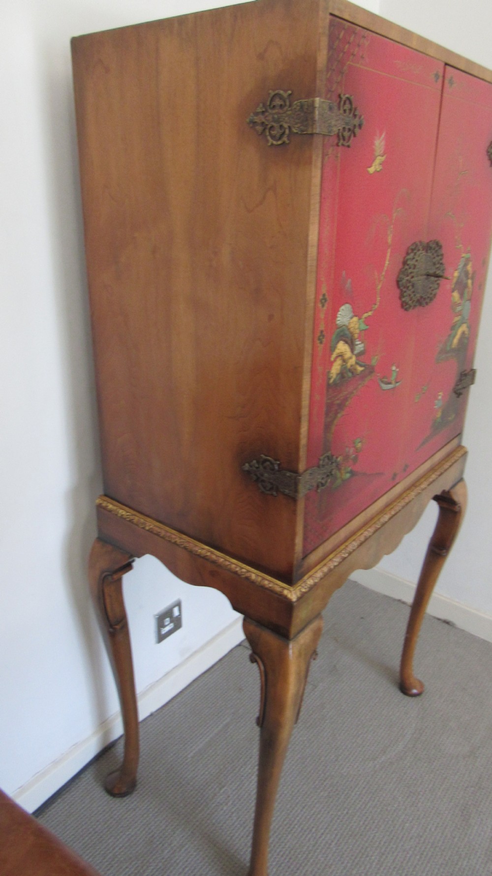 A red lacquered chinoiserie cocktail cabinet decorated with gilt landscapes and figures, featuring ornate brass hinges and set on a carved timber stand with cabriole legs. View XVII