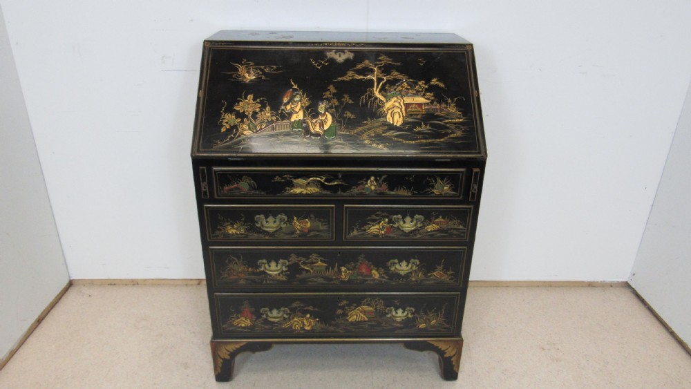 A black lacquered slant-front writing bureau decorated with detailed gold chinoiserie figurative landscapes and fitted with multiple drawers.