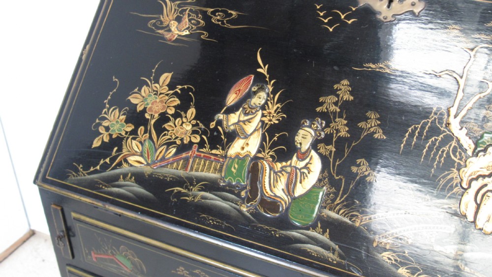 A black lacquered slant-front writing bureau decorated with detailed gold chinoiserie figurative landscapes and fitted with multiple drawers. View II