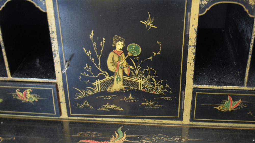 A black lacquered slant-front writing bureau decorated with detailed gold chinoiserie figurative landscapes and fitted with multiple drawers. View IX
