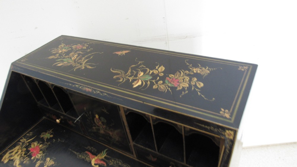 A black lacquered slant-front writing bureau decorated with detailed gold chinoiserie figurative landscapes and fitted with multiple drawers. View X