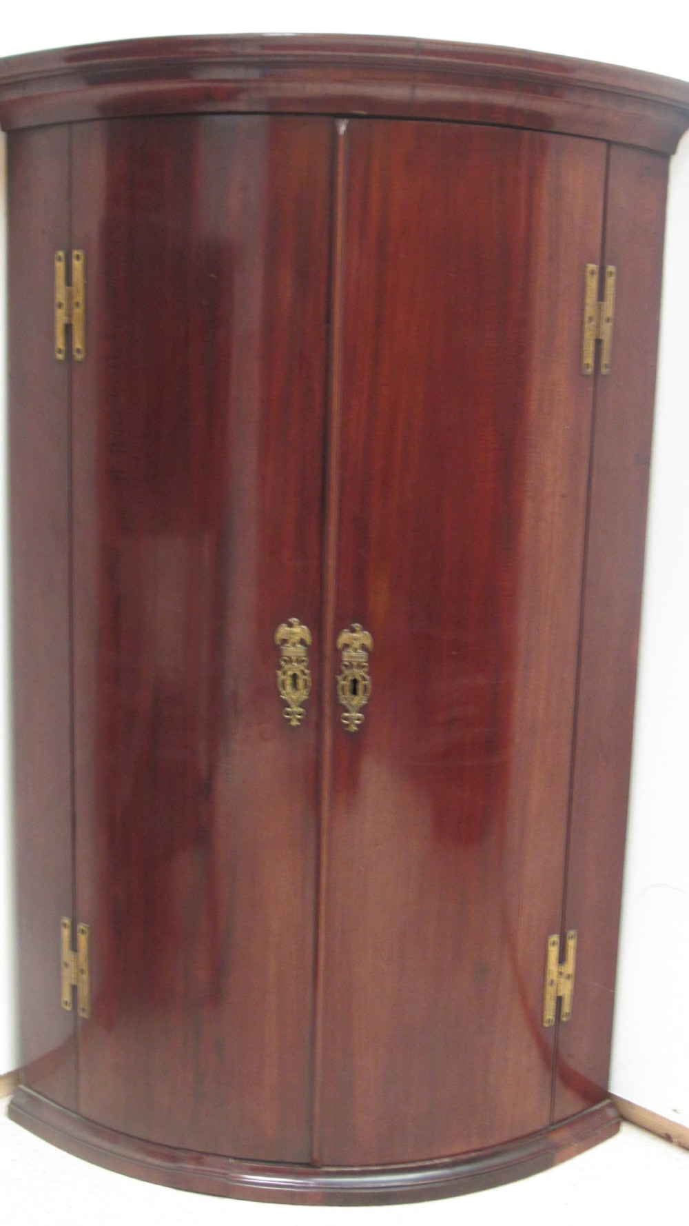 An antique Georgian bowfront corner cupboard crafted from dark mahogany with twin doors, brass H-hinges, and decorative escutcheons. View II