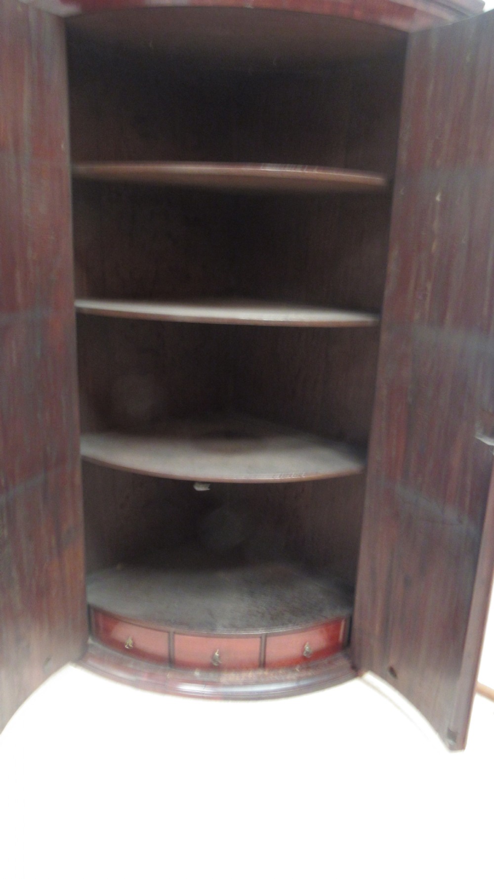 An antique Georgian bowfront corner cupboard crafted from dark mahogany with twin doors, brass H-hinges, and decorative escutcheons. View VI