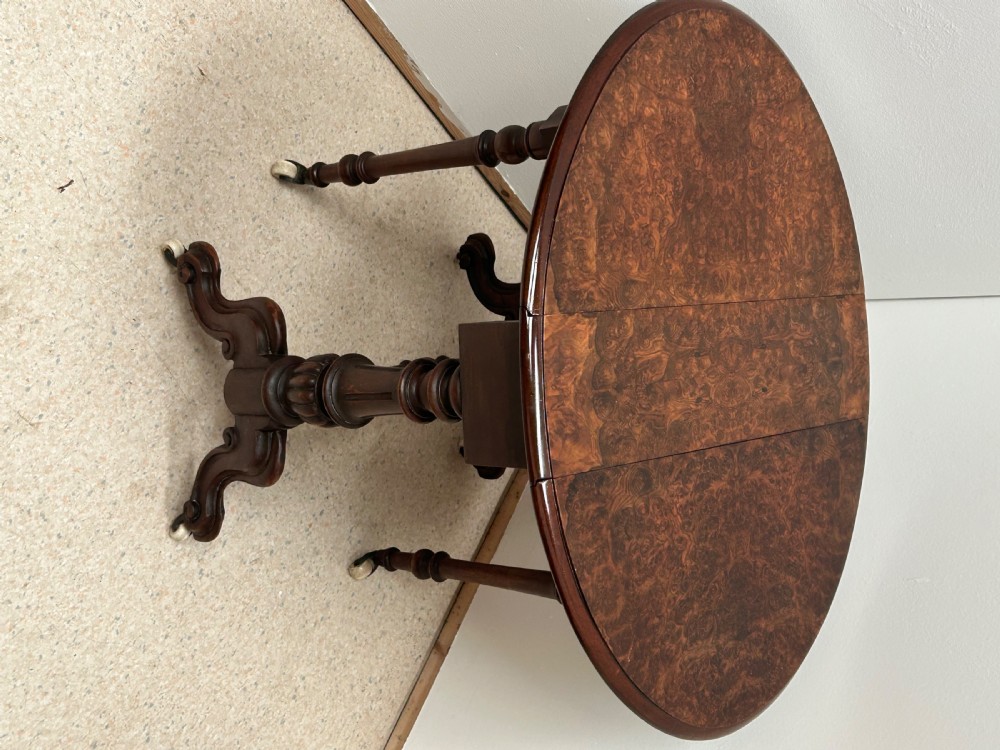 A Victorian burr walnut baby Sutherland drop-leaf side table featuring turned support pillars, carved feet, and ceramic castors. View II