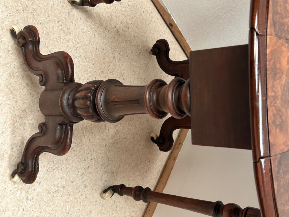 A Victorian burr walnut baby Sutherland drop-leaf side table featuring turned support pillars, carved feet, and ceramic castors. View VI
