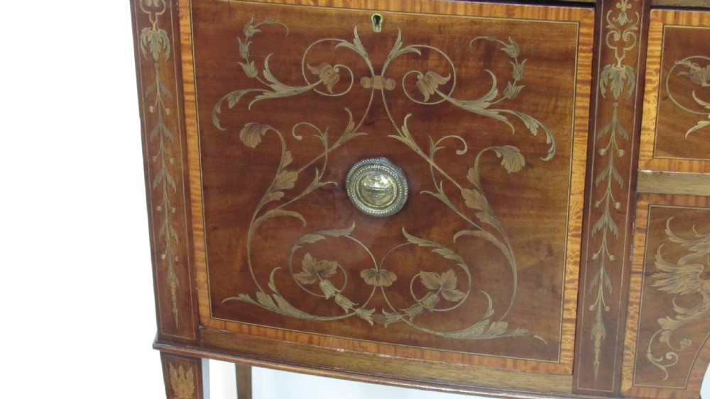 An antique mahogany sideboard with central drawer and side cupboards decorated with fine floral marquetry inlay on tapered legs. View XVI