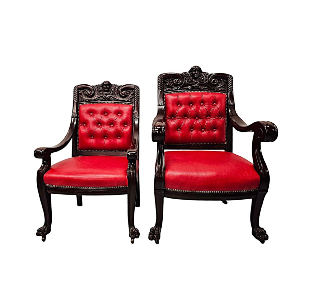 A pair of 19th-century Victorian armchairs in carved dark wood with button-backed red leather upholstery and claw feet.