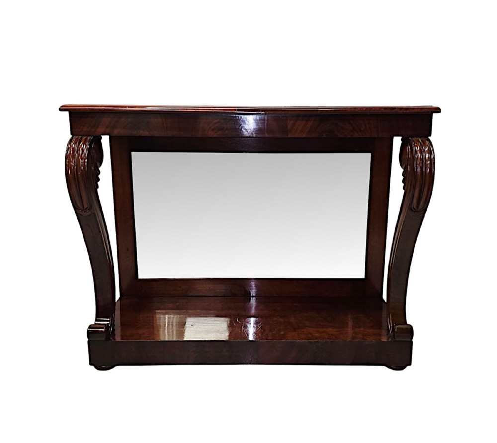 An early nineteenth-century Irish mahogany console table featuring carved scroll legs, an integrated mirror back, and a lower plinth shelf.