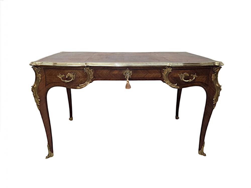 A 19th-century French bureau plat featuring a brown leather writing surface, parquetry veneer, cabriole legs, and gilt-bronze mounts.