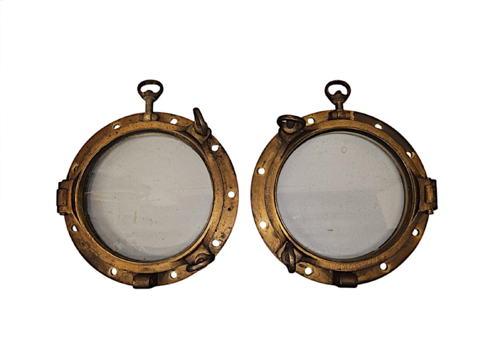 A pair of circular nineteenth-century heavy brass ship portholes with glass panes, hinged frames, and threaded securing clasps.